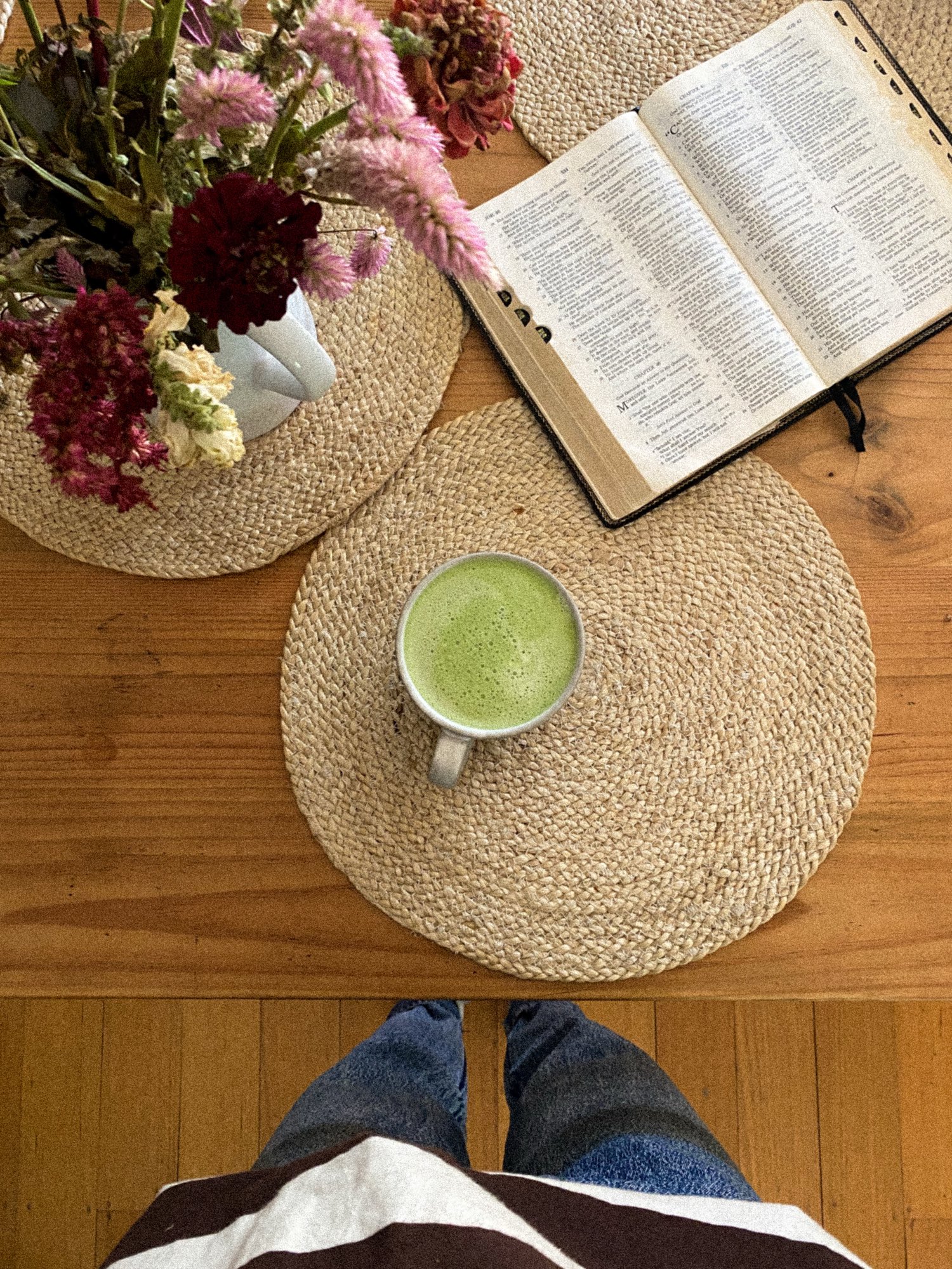 An open Bible, a matcha latte, and fresh flowers on a wood table